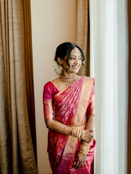 This bride looks absolutely serene. Her hair is styled in a classic South Indian bridal updo, adorned with flowers, and her makeup is subtle yet defining.