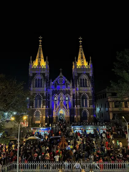A wide night shot of Mount Mary Basilica during Christmas, capturing the festive crowd and the building's grand, illuminated architecture.