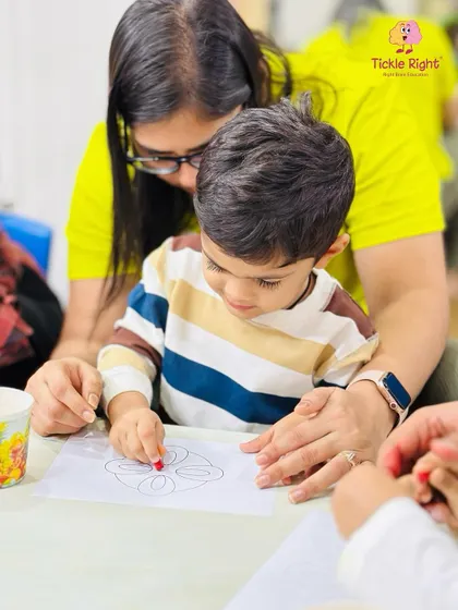 A mother gently guides her son's hand as he colors, a beautiful moment of connection and shared creativity. We encourage parents to be active participants in their child's learning journey.