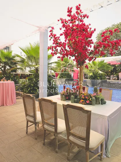 A poolside dining table is decorated with a striking red floral tree centerpiece.