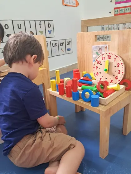 A boy organizes colorful wooden shapes, including cylinders and rings, on a small table. This sorting and stacking activity helps develop skills in categorization and spatial reasoning.