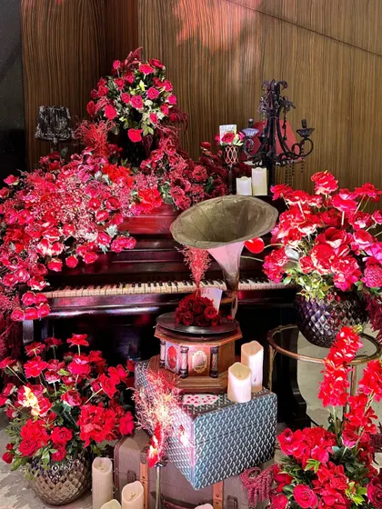 A vintage corner featuring a grand piano and a gramophone, completely surrounded by an explosion of red flowers, creating a dramatic and romantic scene.
