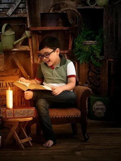A young boy enjoys a book by candlelight in our rustic, vintage-themed studio setup. This moody, warm lighting creates a cozy and nostalgic atmosphere perfect for a child's portrait.