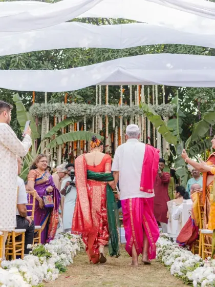 The couple walks down the aisle after their ceremony, surrounded by the vibrant colours of their guests' attire. This photo captures the celebratory atmosphere of the Marathi wedding.