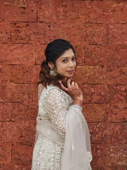 A chic and modern look for a wedding guest. She is wearing a white Anarkali, and her makeup is subtle yet defined, paired with a stylish ponytail.