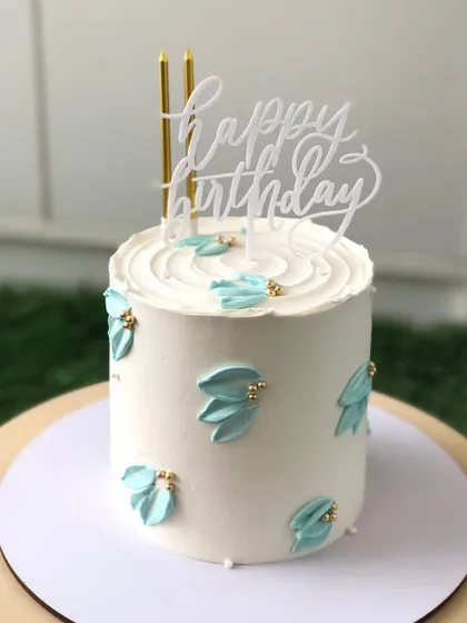 A minimalist cake with simple, elegant blue buttercream strokes and gold bead accents.