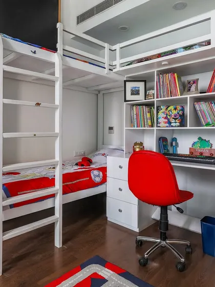 A space-saving solution for a shared kids' room. This custom-built white bunk bed includes an integrated study desk and bookshelf, making it a complete unit for sleep, study, and storage.