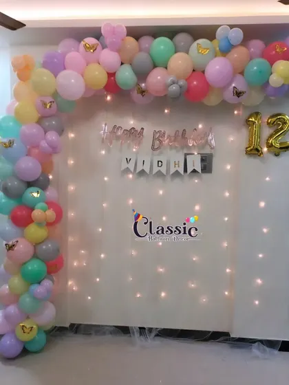 A pastel-colored balloon arch with a fairy light curtain, perfect for a 12th birthday party at home.