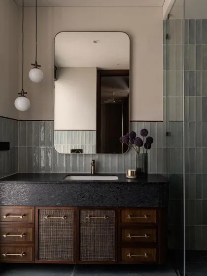 A stunning bathroom featuring a custom vanity with woven details. The combination of the dark stone counter, blue-green tiles, and modern lighting is one of our favorite palettes.