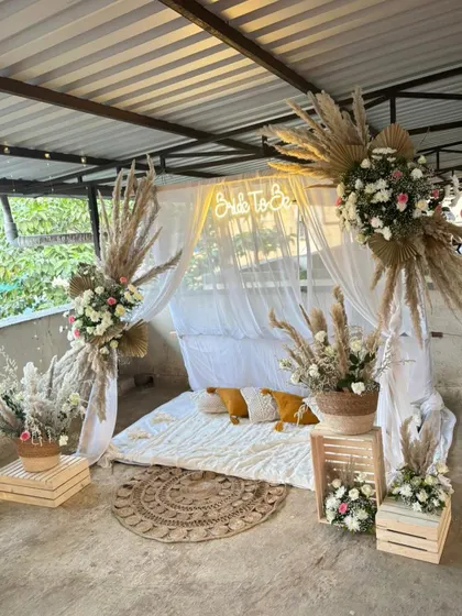 A dreamy, Pinterest-worthy bridal shower with a boho theme. The setup includes a canopy of white drapes, pampas grass arrangements, and a cozy floor seating arrangement.
