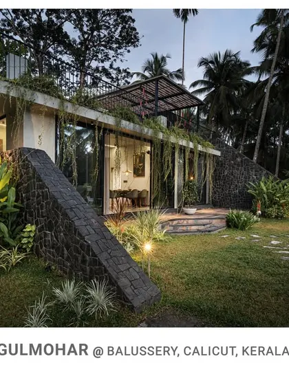 An evening shot of Gulmohar, where landscape lighting accentuates the textures of the stone walls and the lush greenery, creating a magical and serene atmosphere.