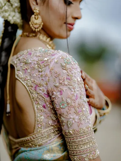 A close-up on the sleeve of the bride's blouse, showing the detailed floral embroidery in shades of pink and green on a sheer fabric.