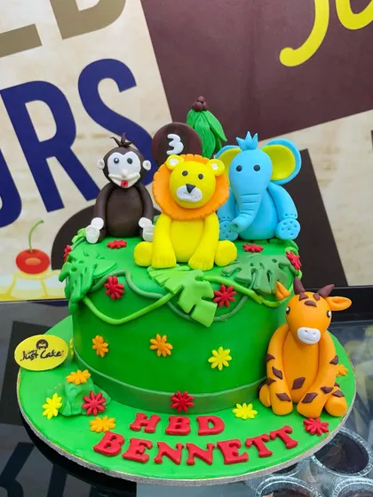 A vibrant green 2.5kg jungle cake with a variety of colorful fondant animals and flowers.