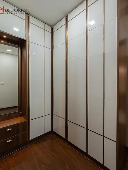 A custom L-shaped hinged wardrobe in a white and wood finish, designed to fit perfectly into a corner. This solution maximizes storage and includes an integrated dressing mirror and drawers.