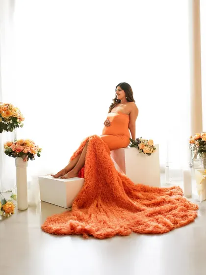 A beautiful portrait of a mother-to-be seated like a queen, her vibrant orange gown cascading around her.