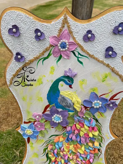 A close-up of a sculpted peacock, focusing on the details of its face and the surrounding purple flowers with pearl centers.