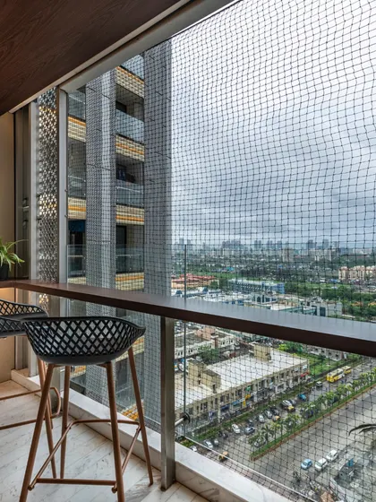 This cozy balcony in The Filigree House features a bar-height counter and stools, offering a perfect spot to enjoy the city view. The space is enclosed with safety netting, making it a practical and serene urban retreat.