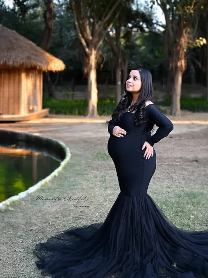 A serene outdoor portrait. The mom-to-be in a classic black gown stands by the water, creating a peaceful and beautiful image in natural surroundings.