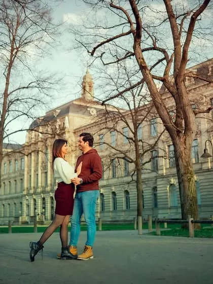 A wide shot of a couple in a loving pose against a backdrop of classic European architecture and bare winter trees.