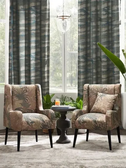 This living room scene uses botanical-print chairs and lush plants to create a tropical, biophilic design theme. The composition shows how to layer patterns and textures for a cohesive, nature-inspired interior.