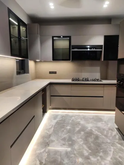 A spacious U-shaped kitchen in a subtle beige matte finish with handleless cabinets. The kick-plate lighting and glass-fronted upper cabinets add a layer of sophistication.