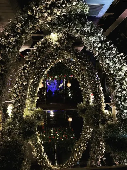 The same floral archway seen at night, with internal lighting that makes the white flowers glow, creating a magical and romantic photo opportunity.