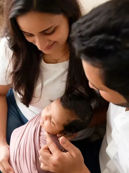 New parents gaze lovingly at their sleeping newborn, who is swaddled and held in their arms.