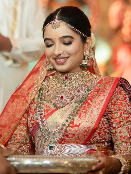 This bride's smile says it all. She looks absolutely stunning in her red and gold Kanchivaram saree, paired with a heavily embroidered custom blouse for her wedding day.
