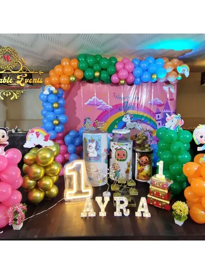 We mixed Cocomelon and Unicorn themes for this colorful first birthday party. The decoration includes a multi-colored balloon arch, character cutouts, and themed plinths.