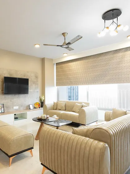 This living room exudes comfort with its plush, beige-colored sofas, a simple TV unit, and large windows that let in plenty of natural light.