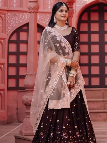 The bride stands gracefully in a palace setting, her deep maroon lehenga and soft makeup creating a look of royal elegance.
