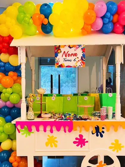 A candy and favor cart for the art party, decorated with a colorful balloon garland and a paint-drip effect, filled with treats for the young artists.