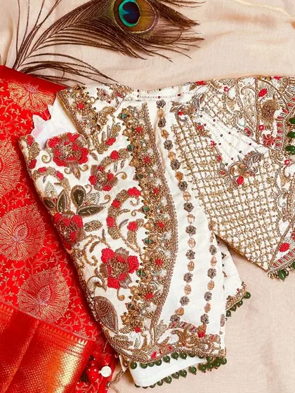 This cream-colored blouse with heavy floral jaal in pearl, bead, and aari work is a must-have for a traditional bride.