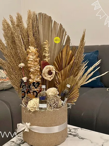 A rustic and sophisticated bouquet for him, featuring dried palms, pampas grass, and miniature alcohol bottles in a stylish jute-covered box.