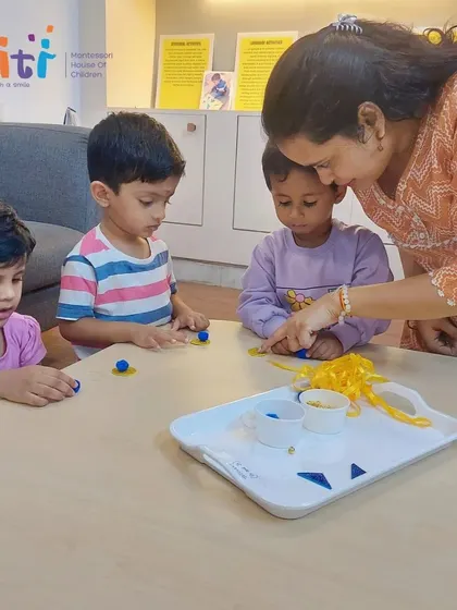 A teacher helps toddlers with a simple Rakhi craft using clay and ribbons. We adapt activities to suit the developmental stage of each child.