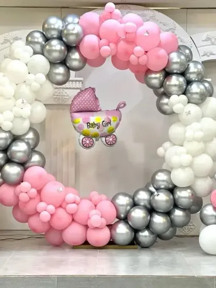A lovely baby shower decoration for a girl. The circular balloon frame in pink, silver, and white is accented with baby girl and carriage foil balloons, perfect for celebrating the little one on the way.