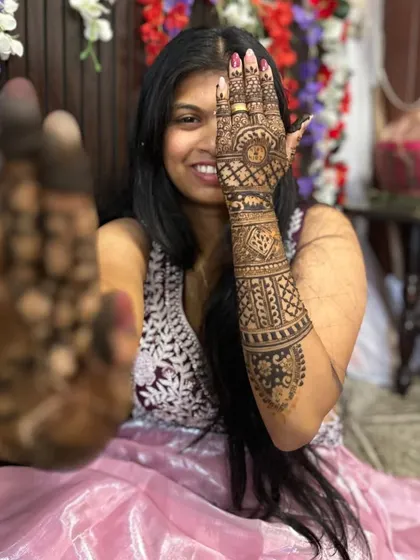 A playful pose from a bride showing off her henna. One hand displays the fresh, dark paste, while the other shows the intricate design on the back of the hand.