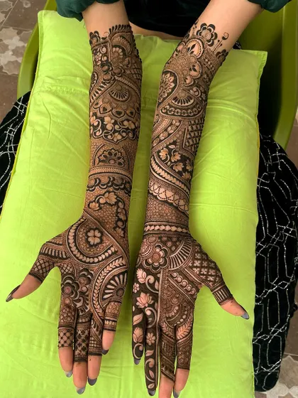 A complete bridal mehndi look, with arms resting on a pillow, showcasing the full extent of the detailed artwork.