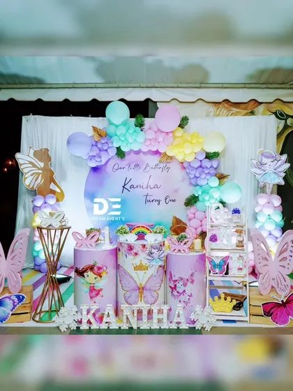 A beautiful outdoor butterfly and fairy-themed party. The watercolor-style backdrop is framed by a pastel balloon garland, perfect for a dreamy first birthday celebration.