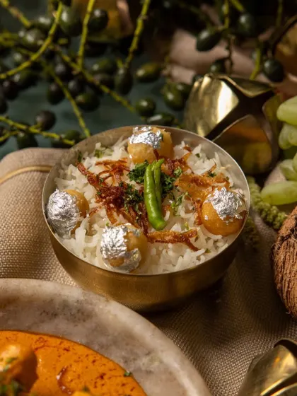 Our festive biryani from the 'RUMI' menu, served in a traditional brass bowl and garnished with fried onions, green chili, and silver leaf vark.