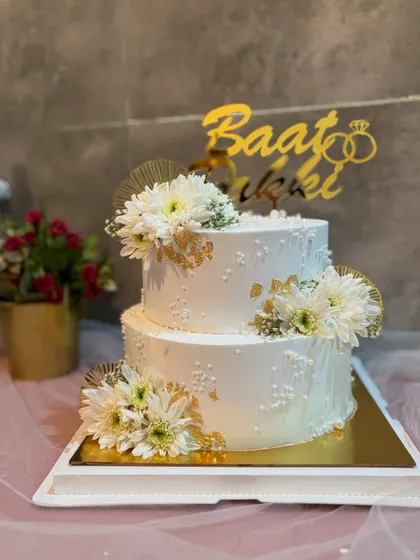 A full view of the elegant two-tier Baat Pakki cake, showcasing its balanced design with fresh white flowers and gold accents.