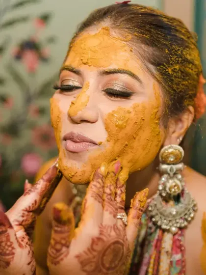 A beautiful close-up of the bride as haldi is applied to her face. Her calm expression and the focus on the texture of the paste make for an artistic and sensory shot.