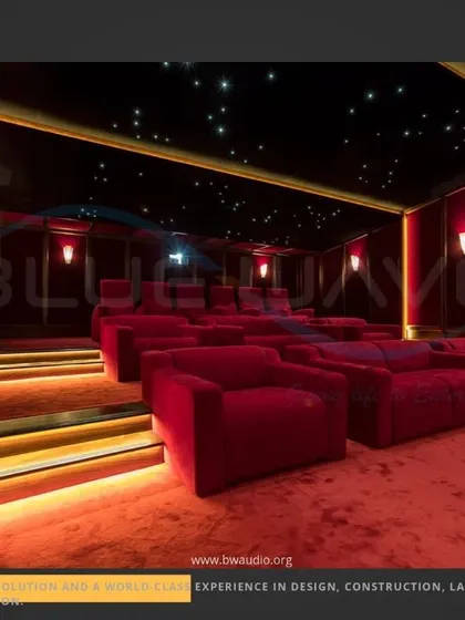 A side view of a grand cinema room, highlighting the tiered seating arrangement with step lighting. The combination of red fabric walls, plush seating, and a starlight ceiling delivers a complete and authentic movie theater experience.