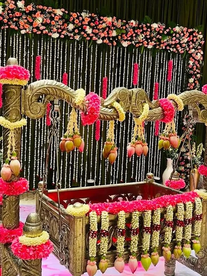An elegant naming ceremony setup with a beautifully decorated cradle. The backdrop features hanging strings of jasmine and pink floral accents, creating a delicate and charming atmosphere.