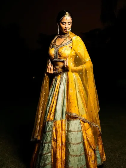 A low-light, dramatic shot of a model in a yellow and grey lehenga. The lighting from above creates a moody, ethereal feel, perfect for an editorial look.