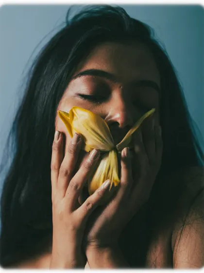 A sensory moment captured as the model smells a flower, her eyes closed in enjoyment.