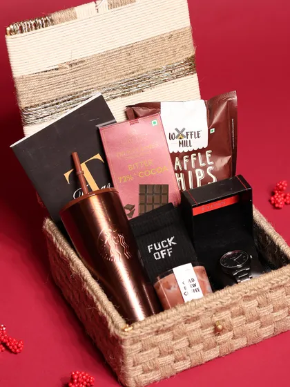 A luxury Christmas hamper for him, presented in a rustic jute-woven box. It includes a Starbucks tumbler, a watch, gourmet chocolate, and a cold brew coffee candle.
