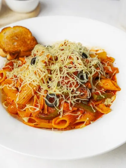 Penne arrabbiata in a rich red sauce, generously topped with cheese and served with garlic toast on a clean white plate.