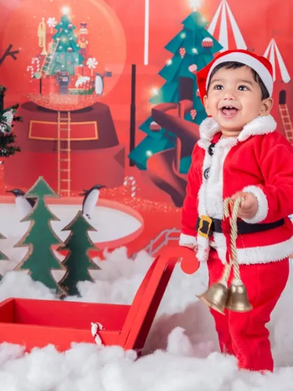 A joyful little Santa, laughing as he stands by his sleigh full of jingle bells.