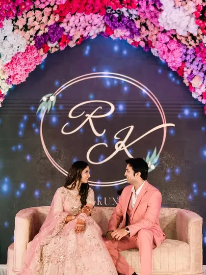 Seated against a backdrop of their elegant monogram and a stunning floral arch, the couple shares a quiet moment. This shot showcases the personalized details and grand scale of a modern engagement stage.